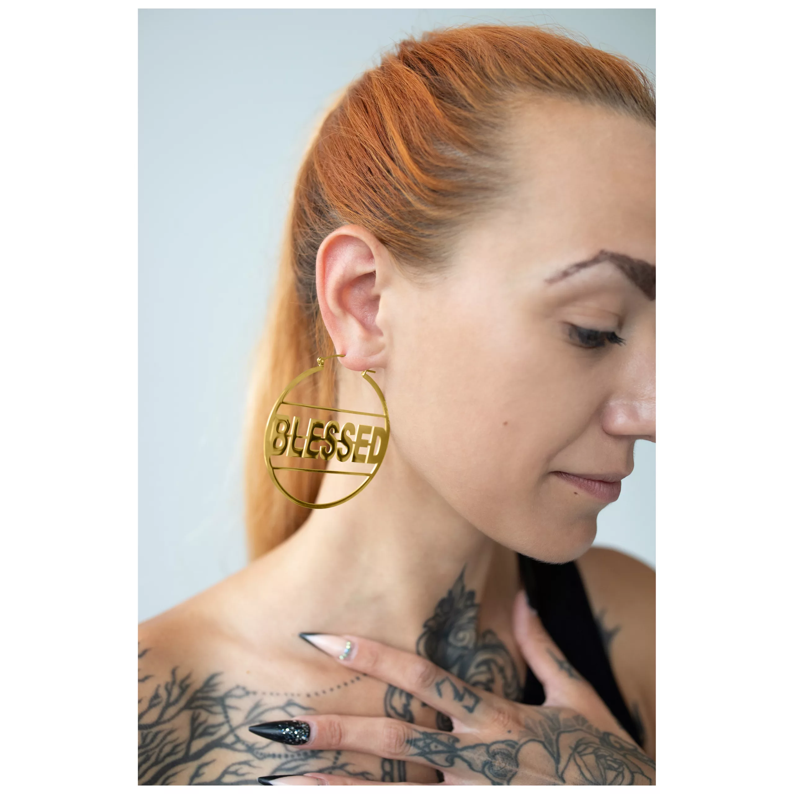 Donna con orecchini Goldene Blessed Hoops e tatuaggi, profilo laterale