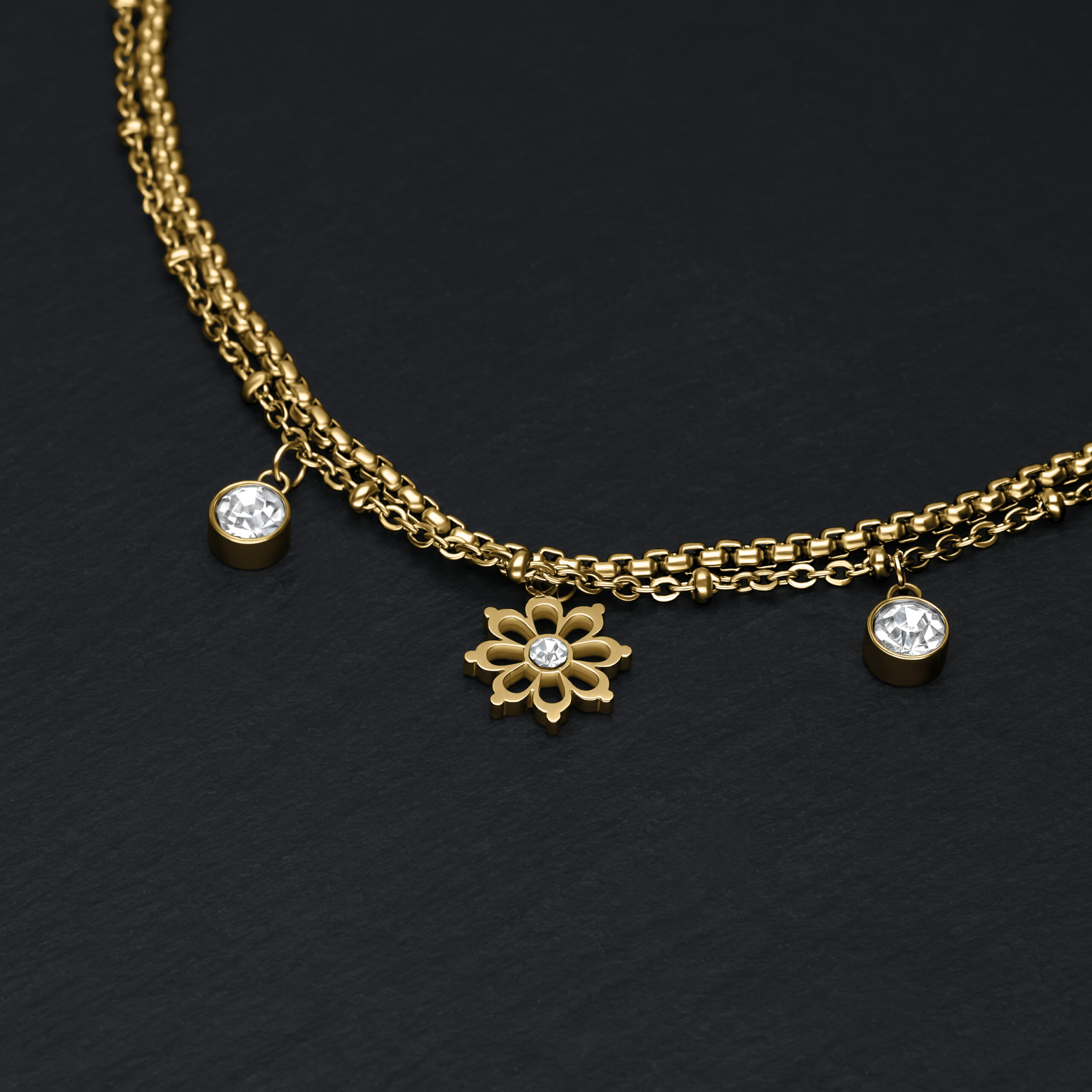 Goldenes Armband mit Blumenanhänger und klaren Kristallen auf schwarzem Hintergrund