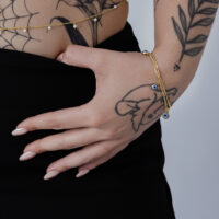 Goldenes Little Nazar Armband am Handgelenk Goldenes Armband mit Nazar-Anhängern an einem tätowierten Handgelenk vor weißem Hintergrund