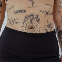 Clicker per ombelico nero con cristalli chiari su pelle con tatuaggi