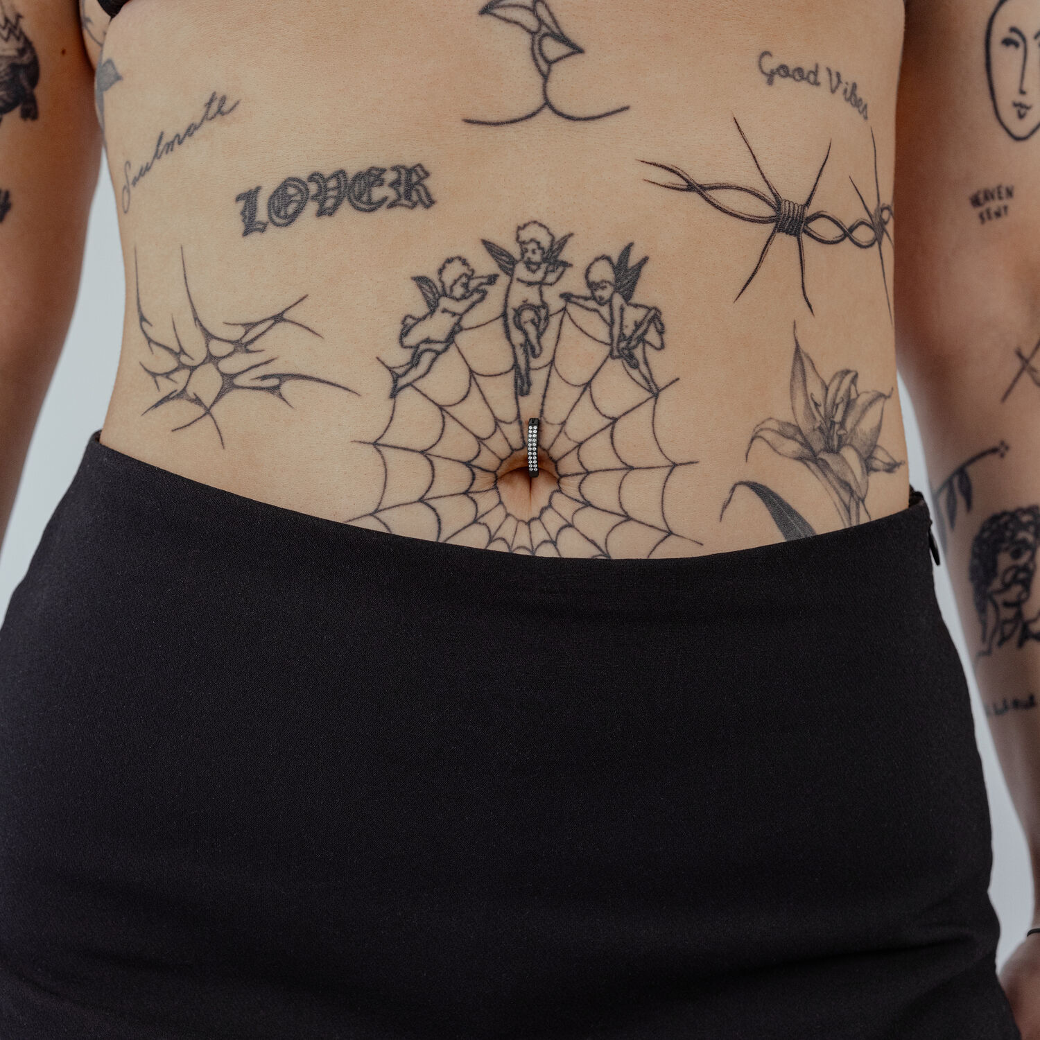 Clicker per ombelico nero con cristalli chiari su pelle con tatuaggi