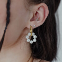 Goldene Creolen mit Perlen an einem Ohr getragen, vor neutralem Hintergrund