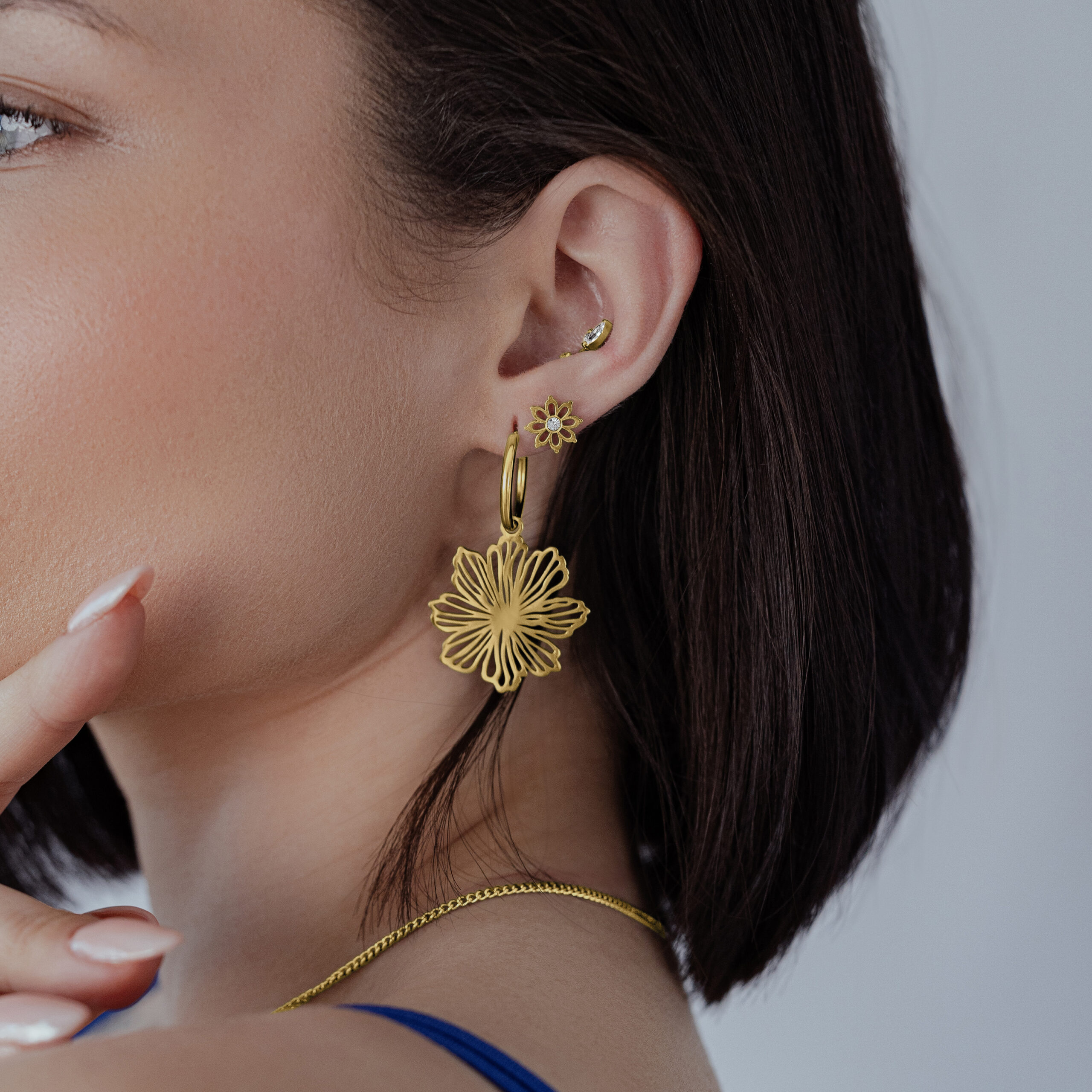 Frau trägt goldene Fine Flower Hoops Ohrringe vor neutralem Hintergrund
