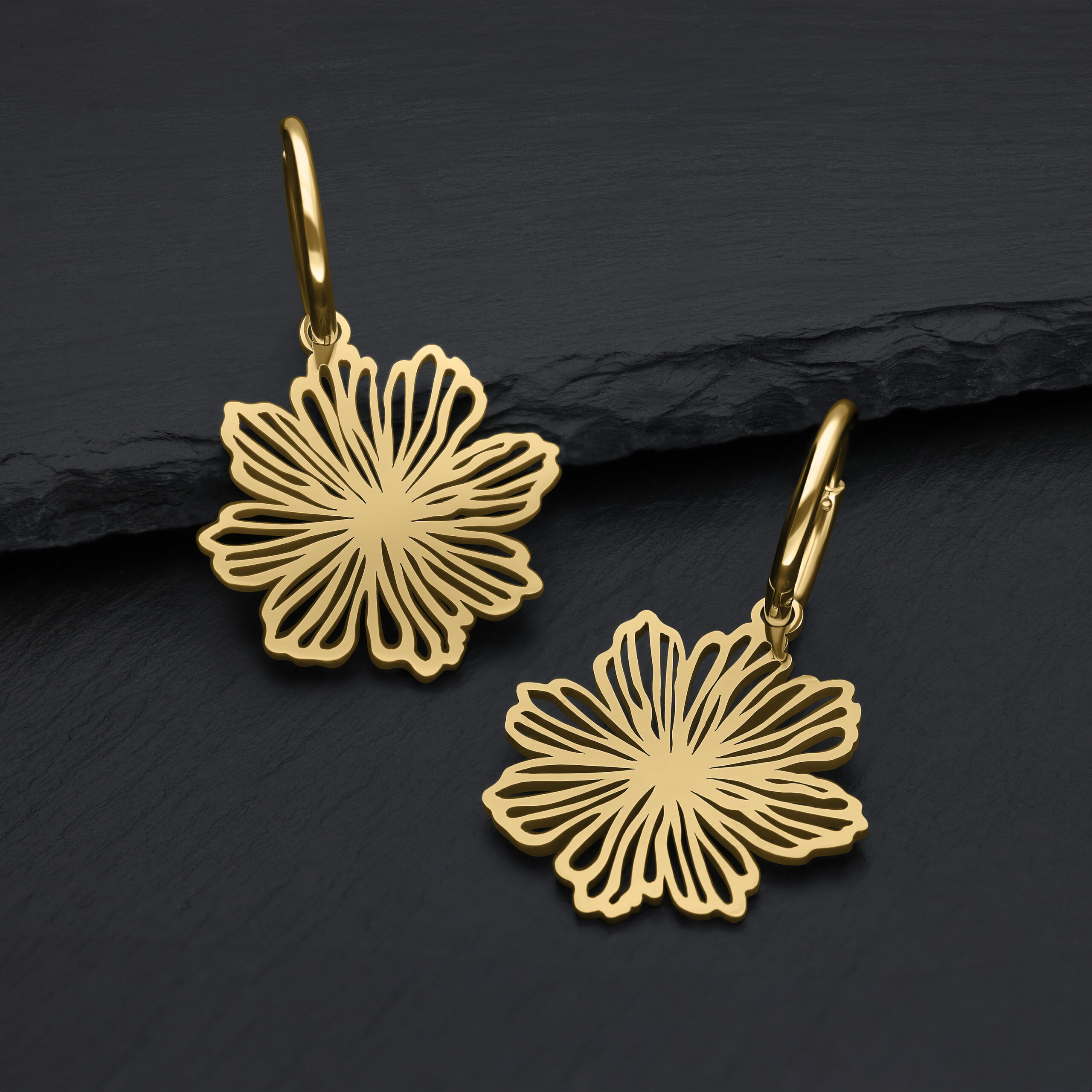 Goldene Ohrhänger in Blumenform auf schwarzem Hintergrund
