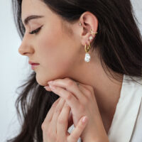 Barocke Perlen-Creolen aus Gold Frau mit goldenen Barocke Perlen-Creolen vor weißem Hintergrund