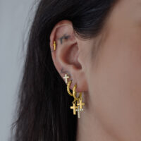 Goldene Ohrringe mit Kreuzanhänger an einem Ohr, seitliche Ansicht