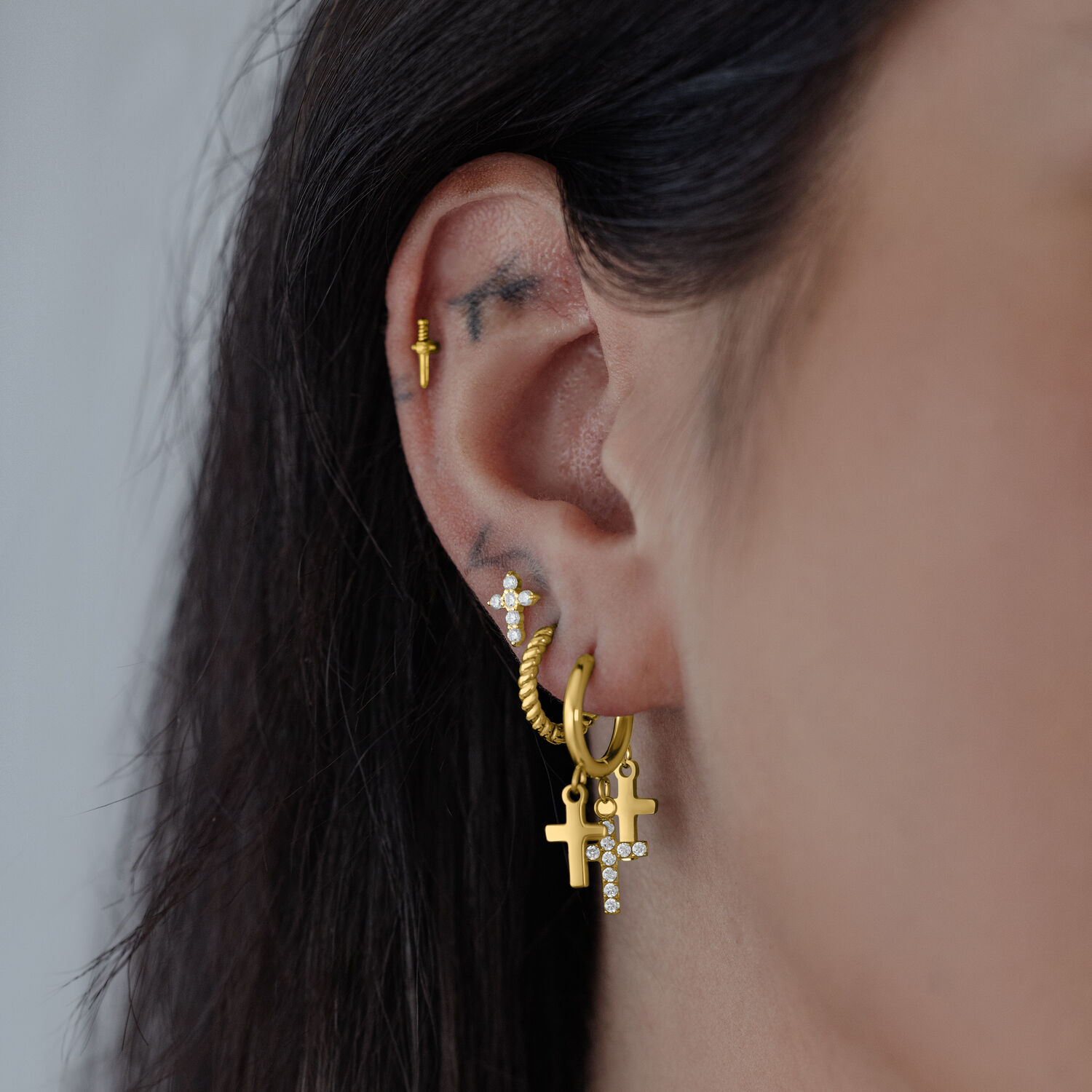 Goldene Ohrringe mit Kreuzanhänger an einem Ohr, seitliche Ansicht