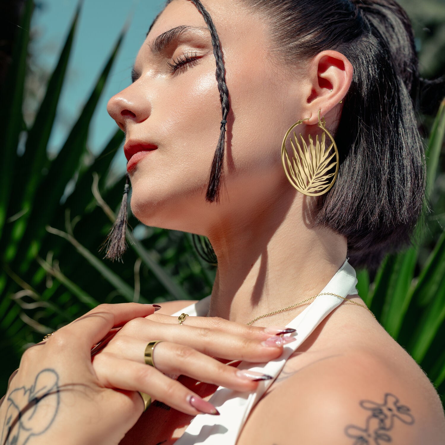 Frau mit goldenen Ohrringen in Blattform, draußen vor grünen Pflanzen