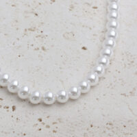 Große synthetische Perlenkette mit goldenen Metallelementen auf hellem Hintergrund