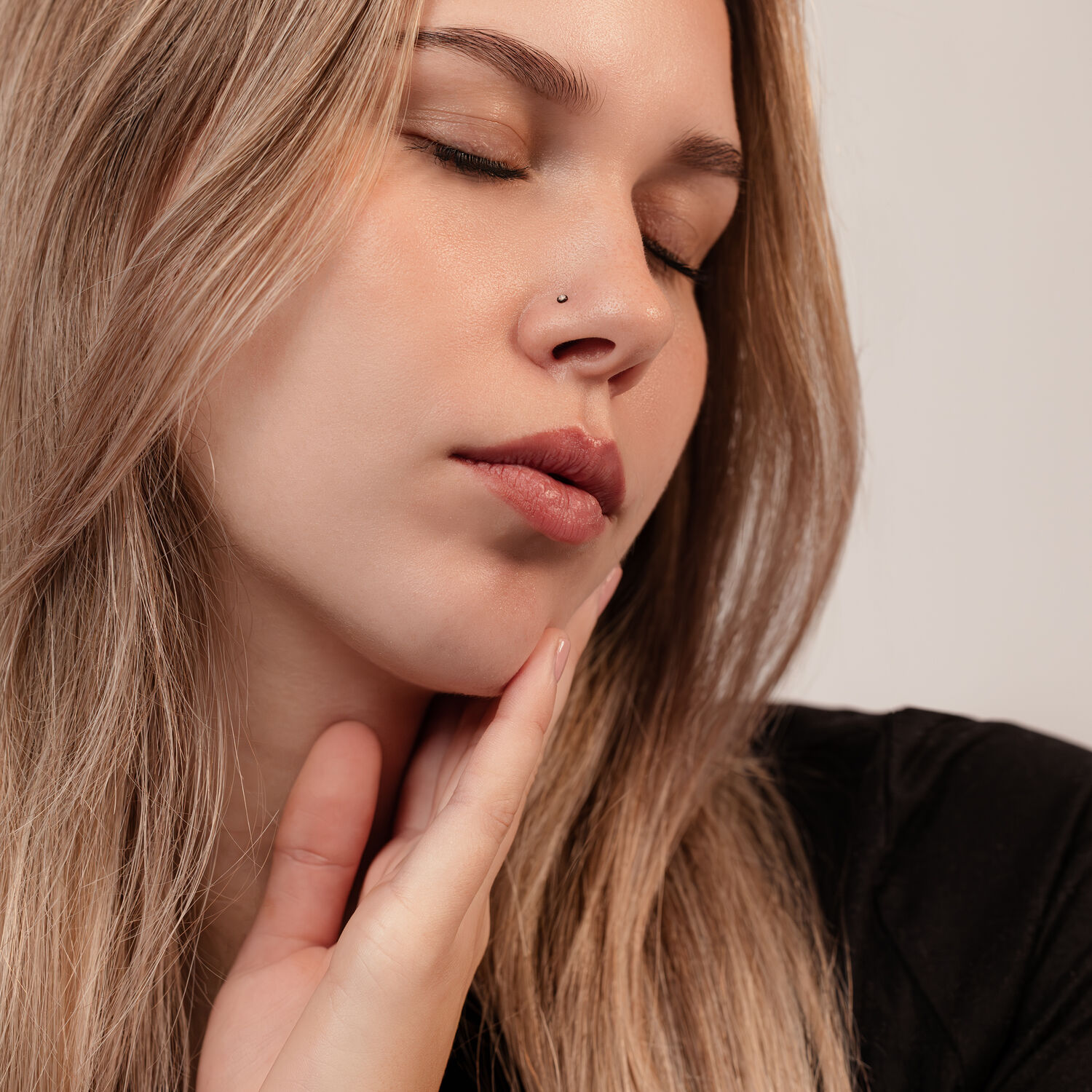 Donna con piercing al naso nero in titanio, occhi chiusi, capelli castano chiaro