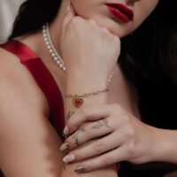 Goldenes Sacred Heart Armband am Handgelenk Frau trägt goldenes Sacred Heart Armband, rotes Kleid, Perlenkette