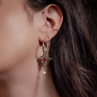 Goldene Creolen mit rotem Herz und Kettenanhänger am Ohr einer Frau