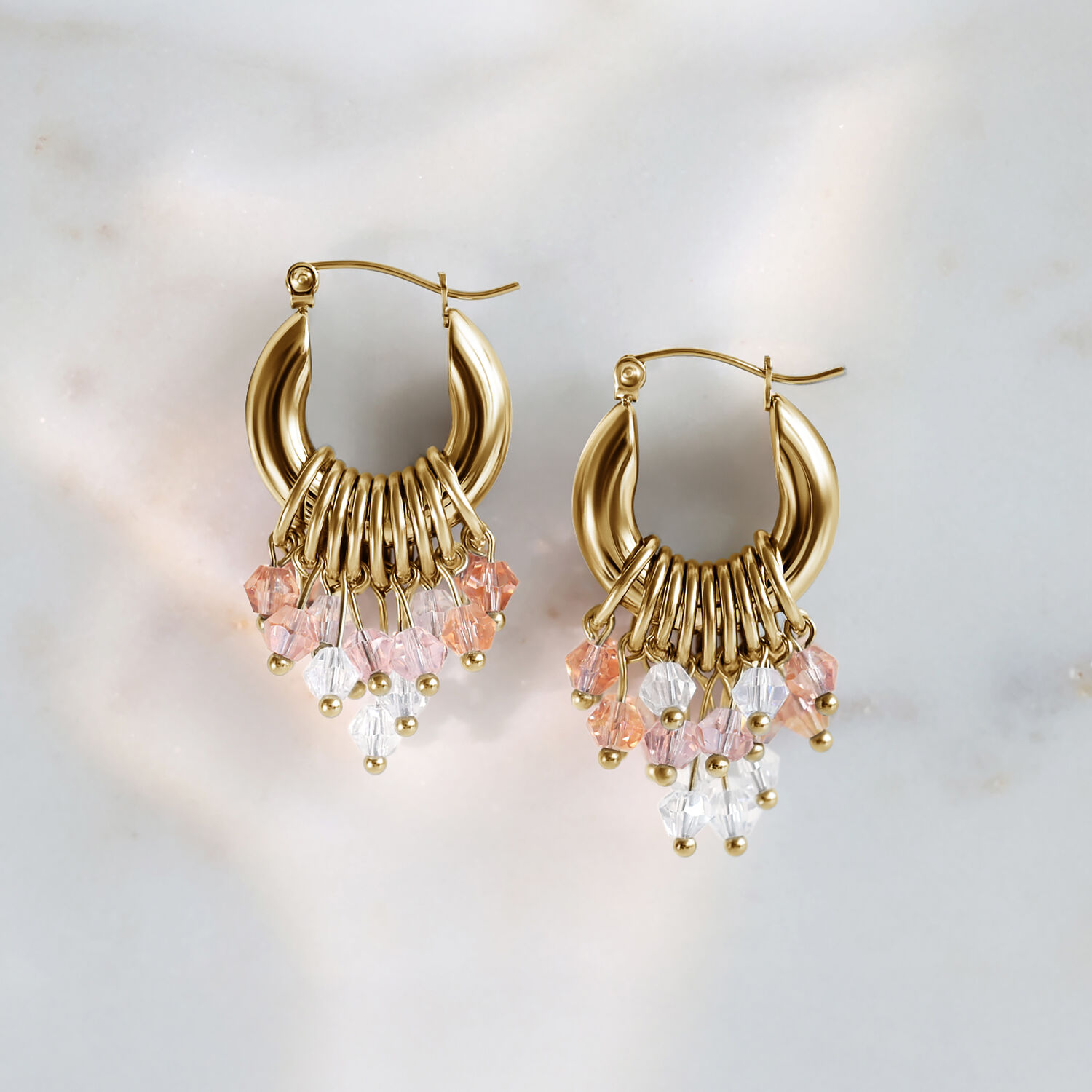 Goldene Glamour Hoops Ohrringe mit rosa und klaren Kristallen auf Marmorhintergrund