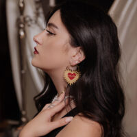 Goldene Herz-Ohrringe mit Stacheldraht in Ohr einer Frau mit dunklem Haar