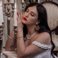 Frau mit goldenen Sacred Heart Ohrringen, rote Lippen, Kerzen im Hintergrund