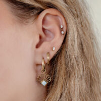 Goldene Creolen mit synthetischem Opal an weiblichem Ohr, blondes Haar