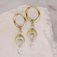 Goldene Creolen mit Kristallanhänger Zwei goldene Creolen auf hellem Stein, mit klarem Kristallanhänger