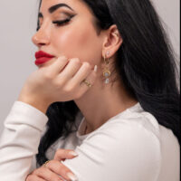 Goldene Creolen mit Kristallanhängern Frau mit goldenen Ohrringen und Kristallanhängern, weißer Hintergrund