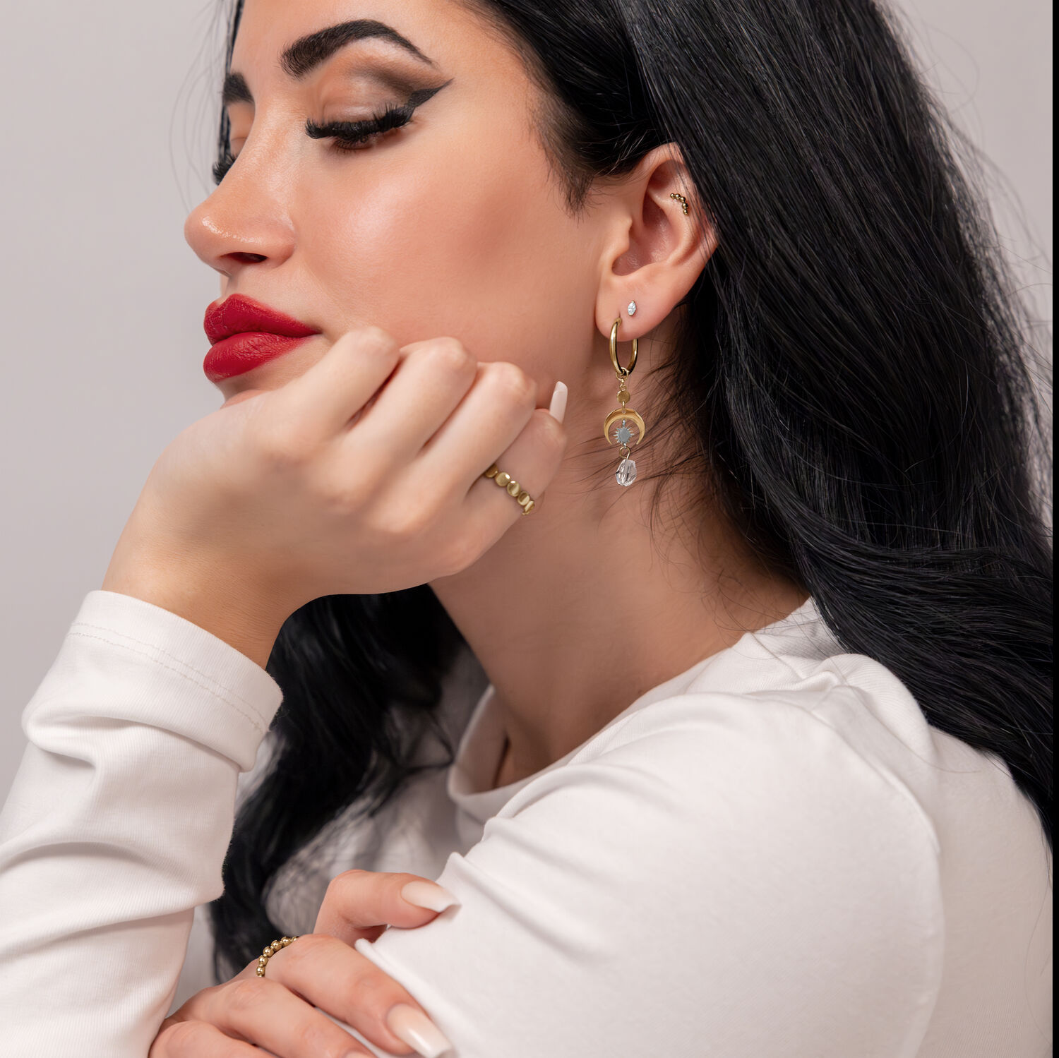 Goldene Creolen mit Kristallanhängern Frau mit goldenen Ohrringen und Kristallanhängern, weißer Hintergrund