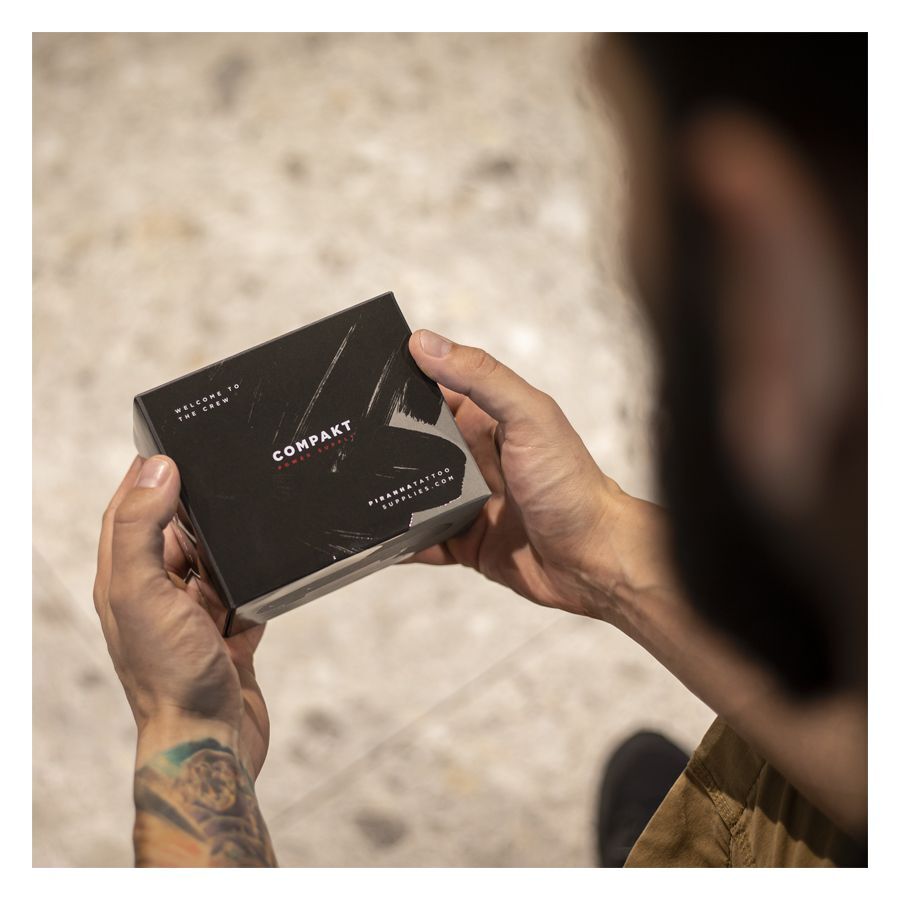 Alimentatore Piranha nero in confezione Uomo tiene confezione di alimentatore Piranha nero con tatuaggio sulla mano